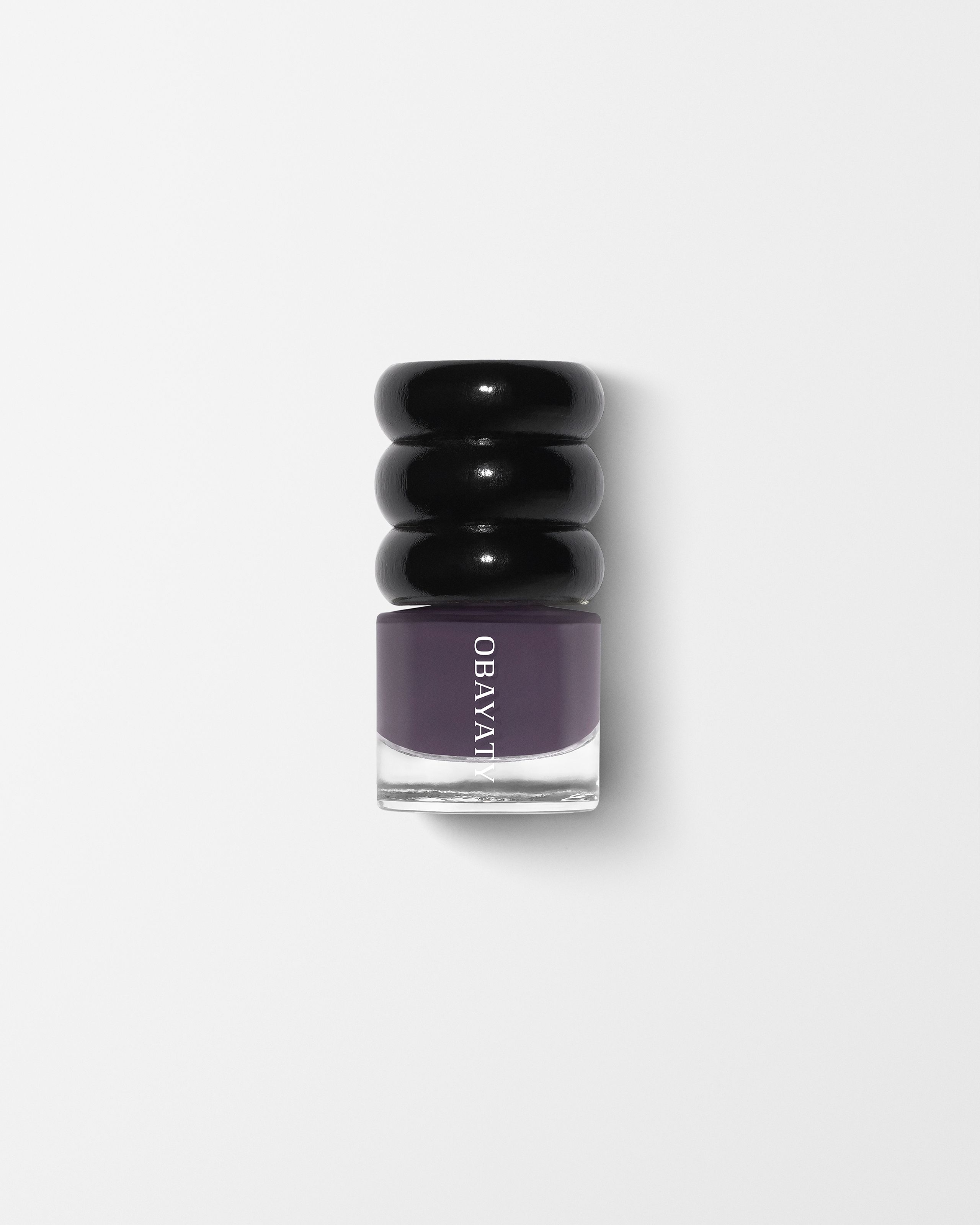 Black wood cap and glass bottle of nail polish in the colorViolet Dusk laying on a grey surface