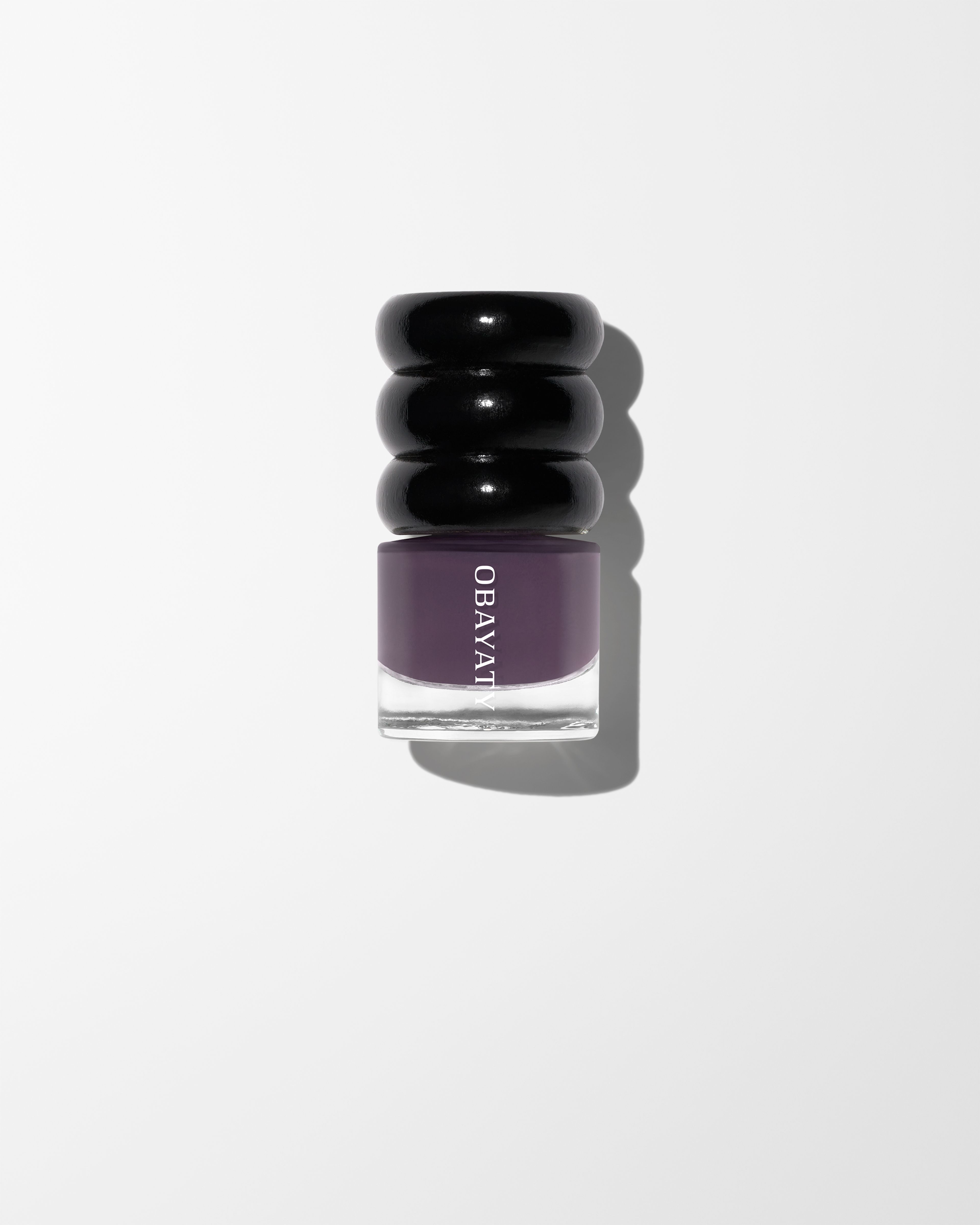 Black wood cap and glass bottle of nail polish in the color Violet Dusk laying on a grey surface