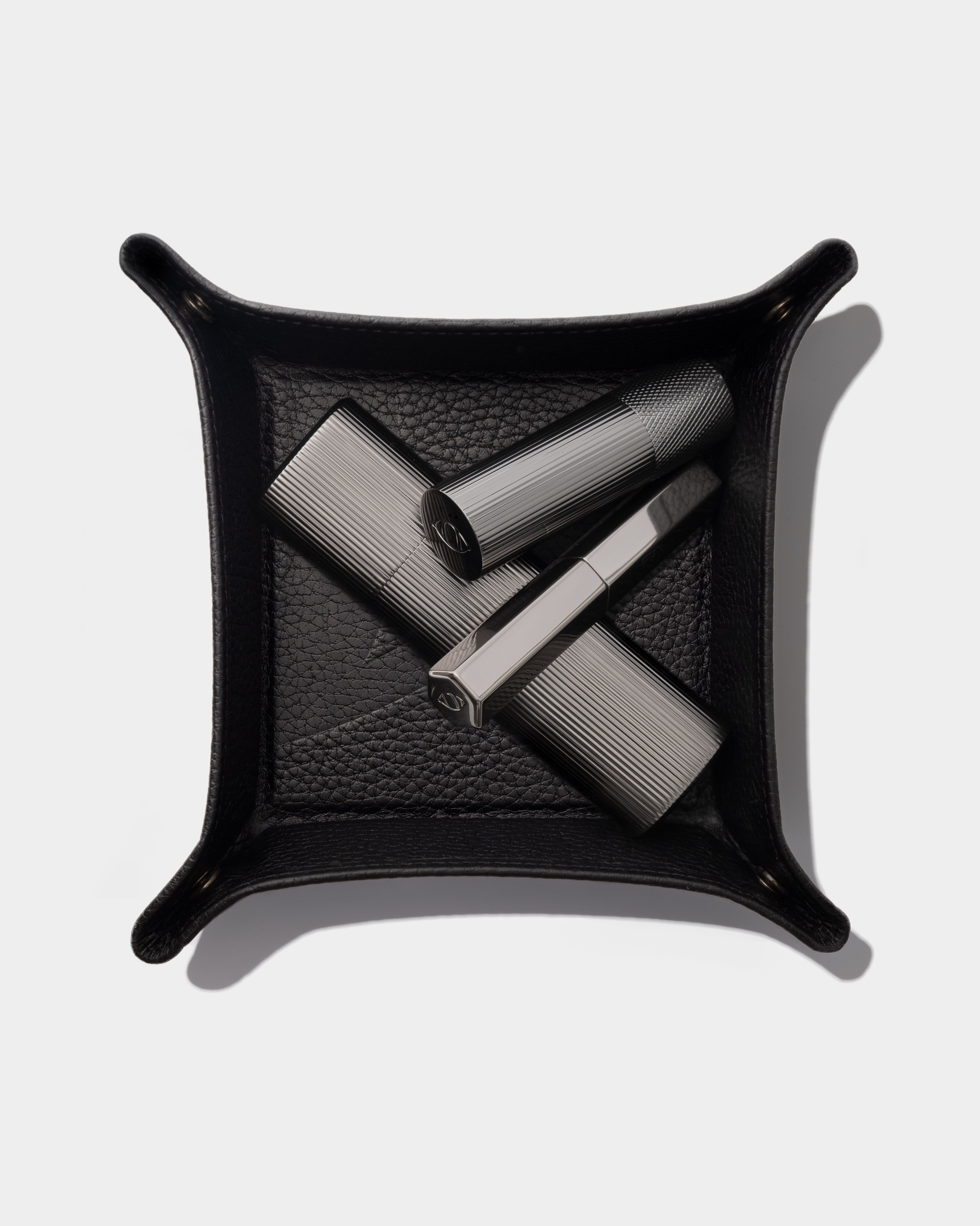 Black leather tray with make up products in it, laying on a grey surface