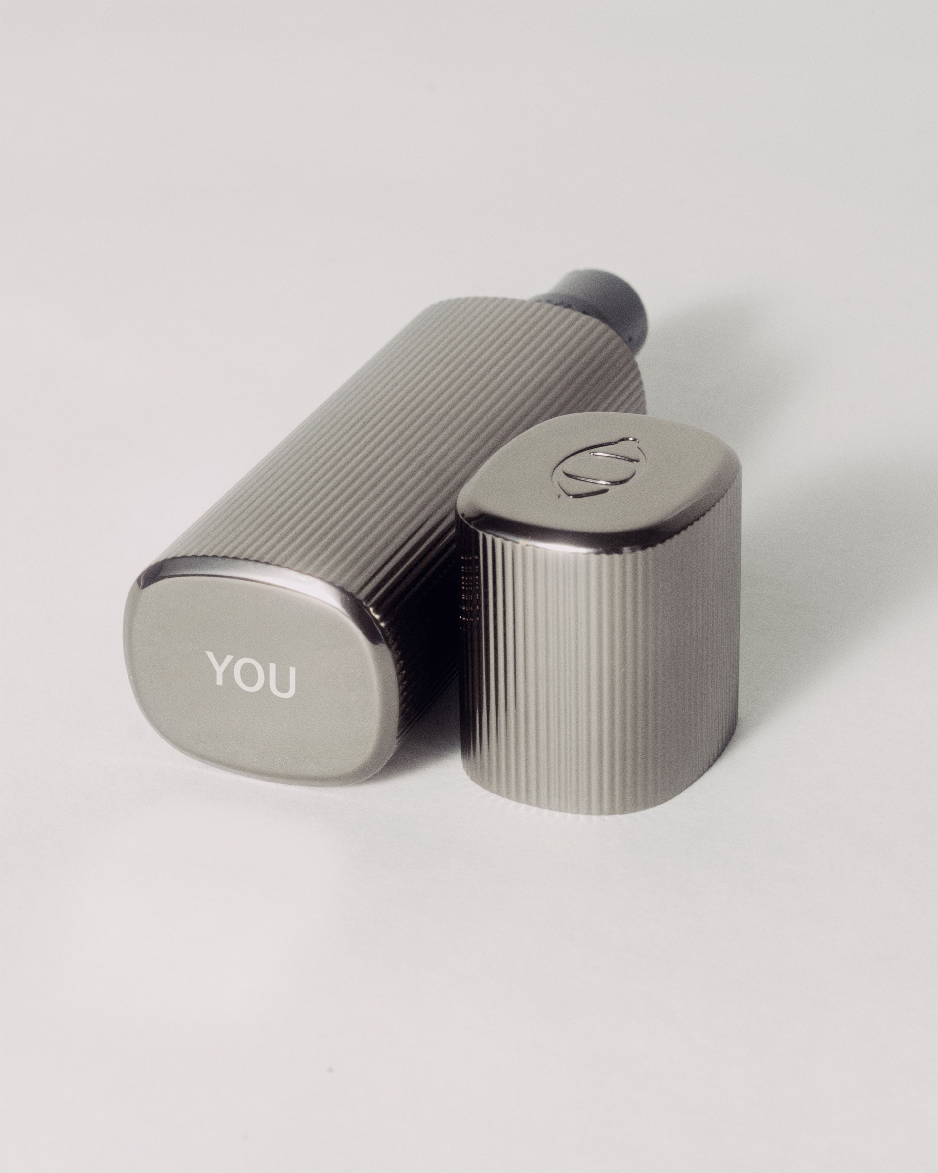 Skin Perfector laying on a grey background with the text "YOU" engraved on the underside