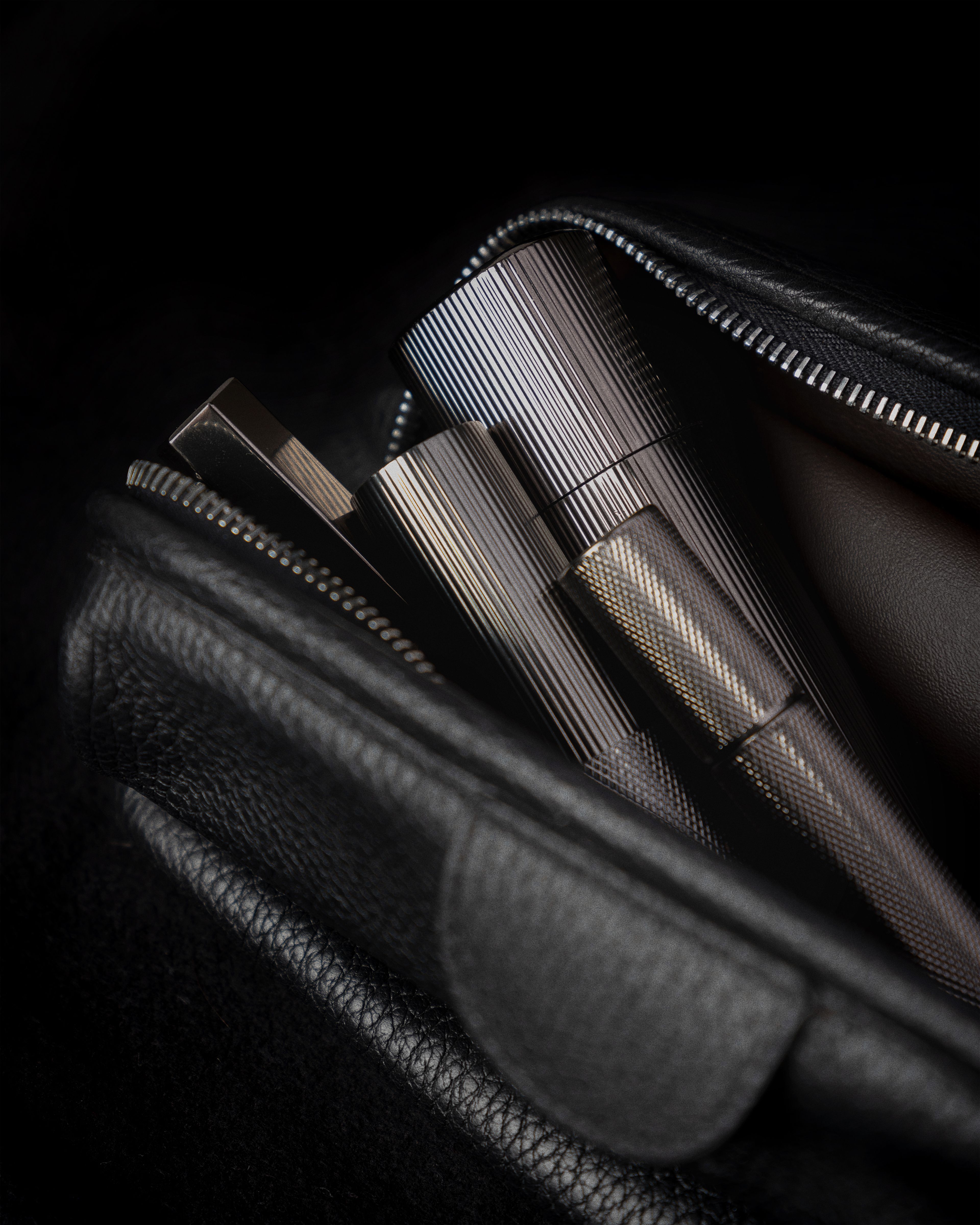 Men's concealer, moisturizer, eye cream and lip balm laying in a black leather toiletry bag.
